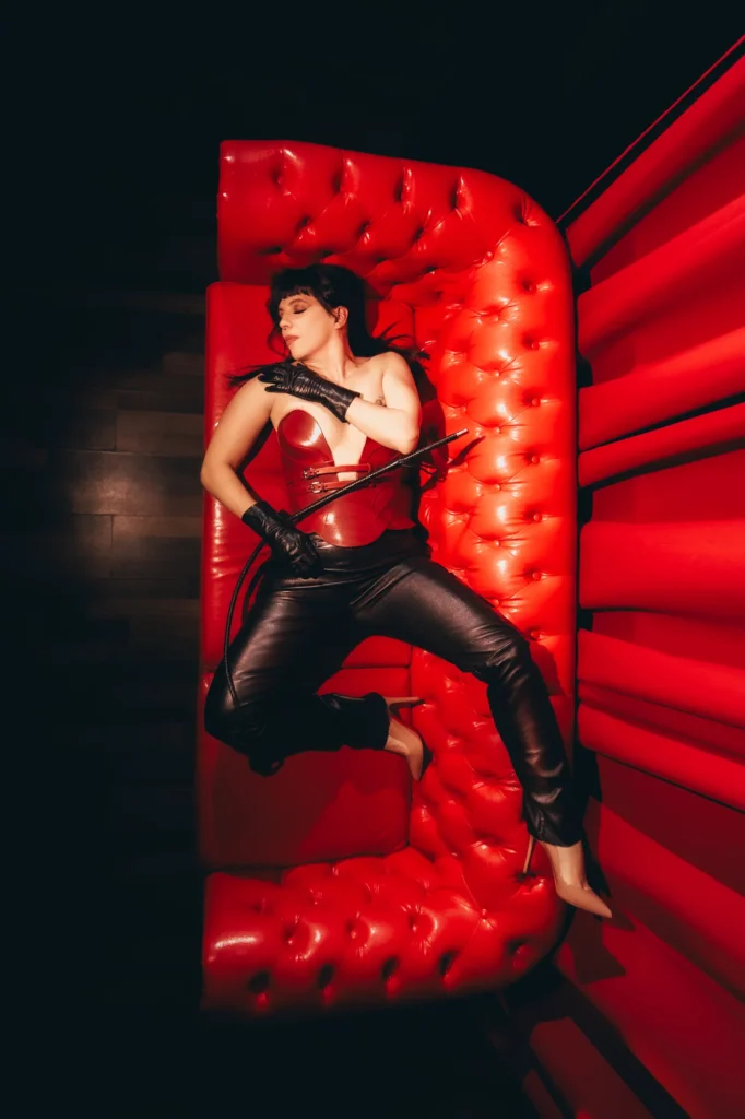 Berlin Domina Lady Vyra in a sculptural pose wearing a red leather corset